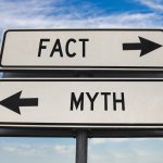 Fact versus myth road sign with two arrows on blue sky background. White two street sign with arrows on metal pole. Two way road sign with text.