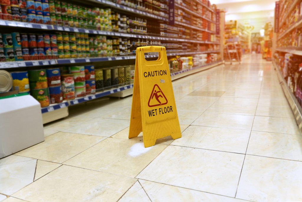 Yellow sign - caution. Wet floor is in the supermarket against the background of blurry products standing on the shelves