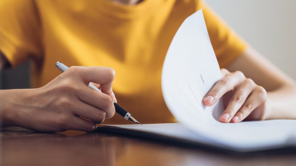 Woman signing document and hand holding pen putting signature at paper, order to authorize their rights.