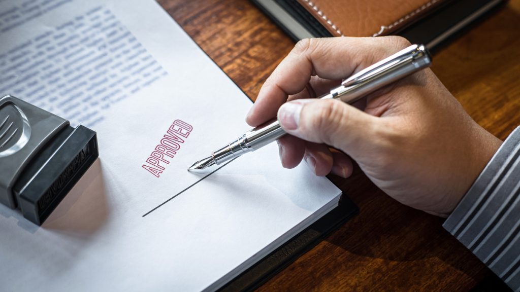 Close up hands of businessman signing and stamp on paper document to approve business investment contract agreement.