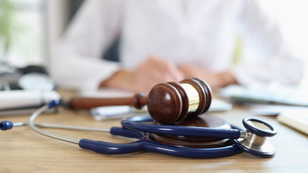 Closeup of judge gavel of stethoscope doctor in background writing notes. Concept of legal aspects of healthcare and medical insurance payments