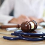 Closeup of judge gavel of stethoscope doctor in background writing notes. Concept of legal aspects of healthcare and medical insurance payments